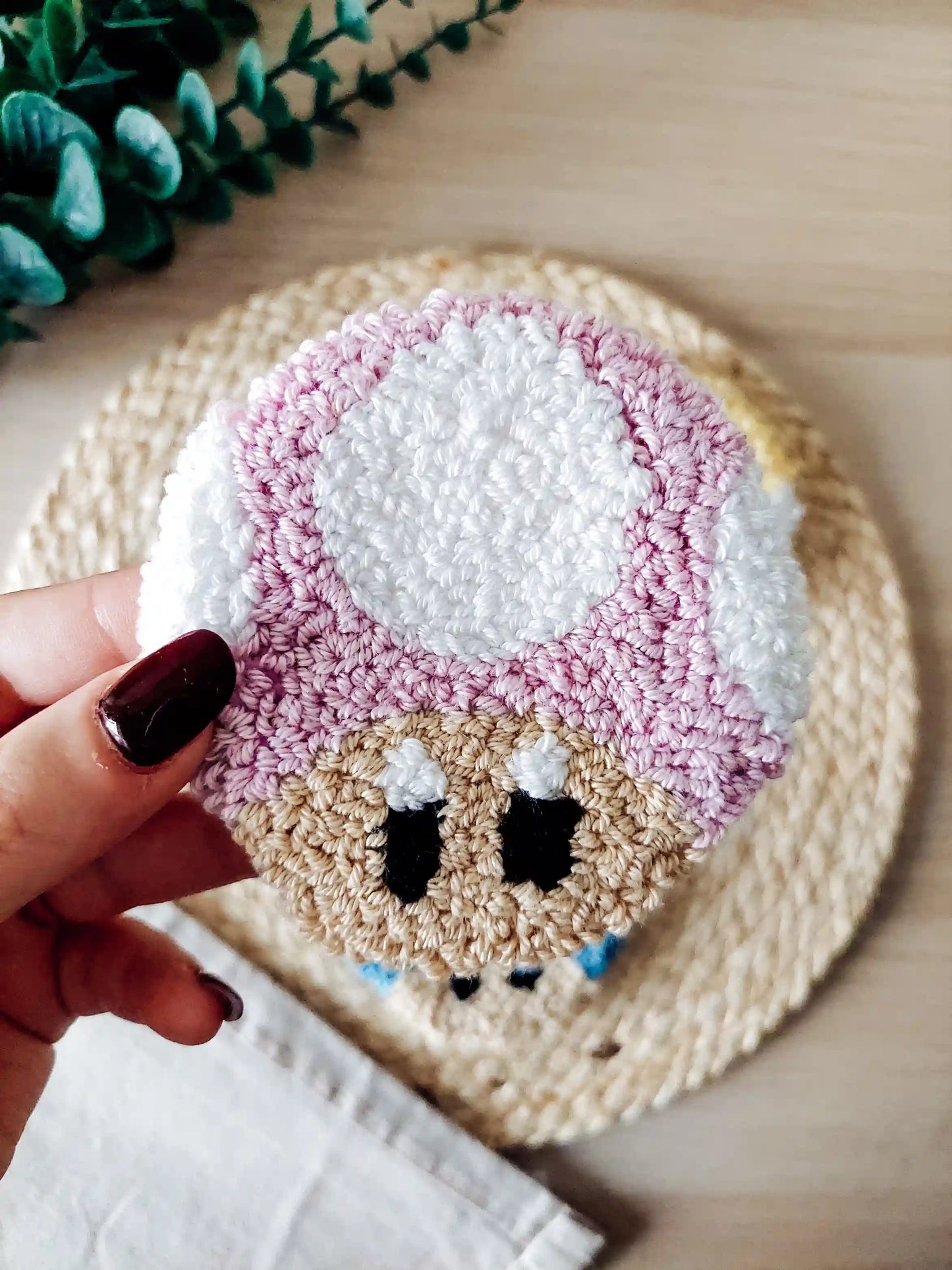 Punch needle mushroom coasters in  lilac, inspired by Toad, displayed on a woven mat with decorative flowers.