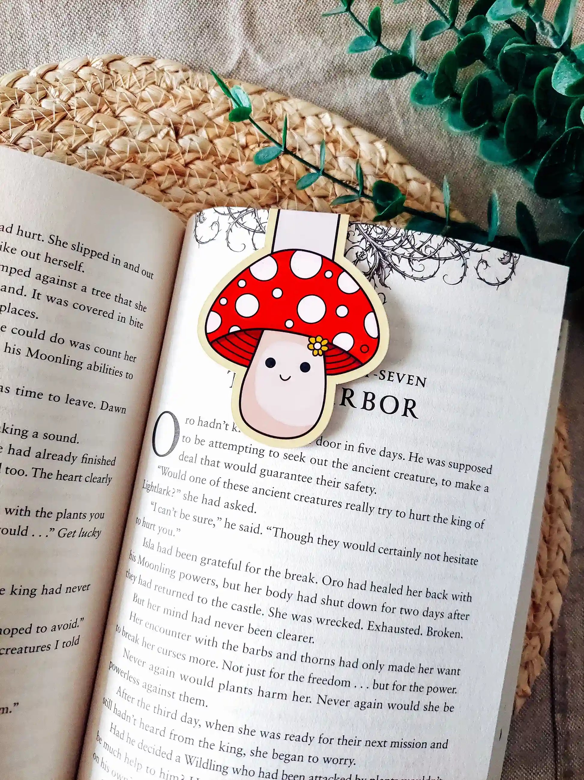 Book with a cute mushroom-shaped magnetic bookmark on an open book, surrounded by green leaves.