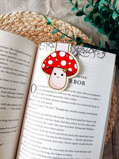 Book with a cute mushroom-shaped magnetic bookmark on an open book, surrounded by green leaves.