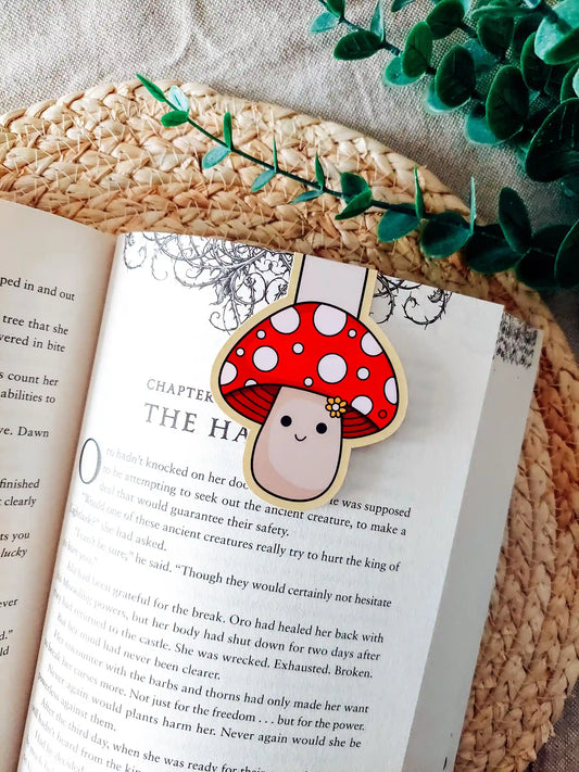 Book with a cute mushroom-shaped magnetic bookmark on an open book, surrounded by green leaves.