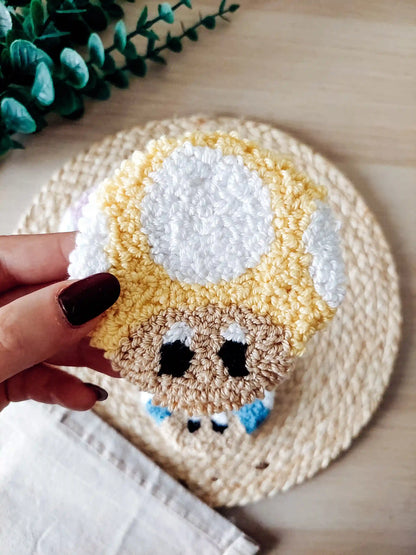 Punch needle mushroom coasters in  yellow, inspired by Toad, displayed on a woven mat with decorative flowers.