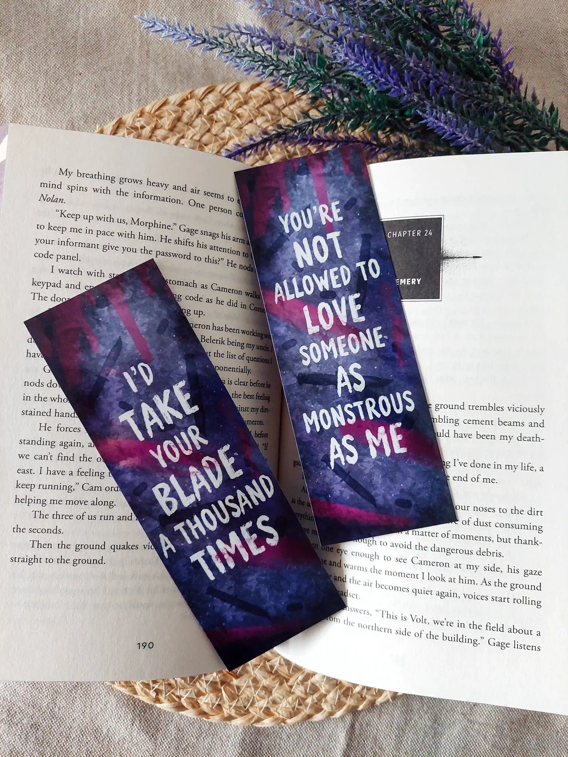 My Blade, Your Back inspired bookmarks displayed on an open book, featuring a purple and pink background with dagger illustrations and white quotes. 