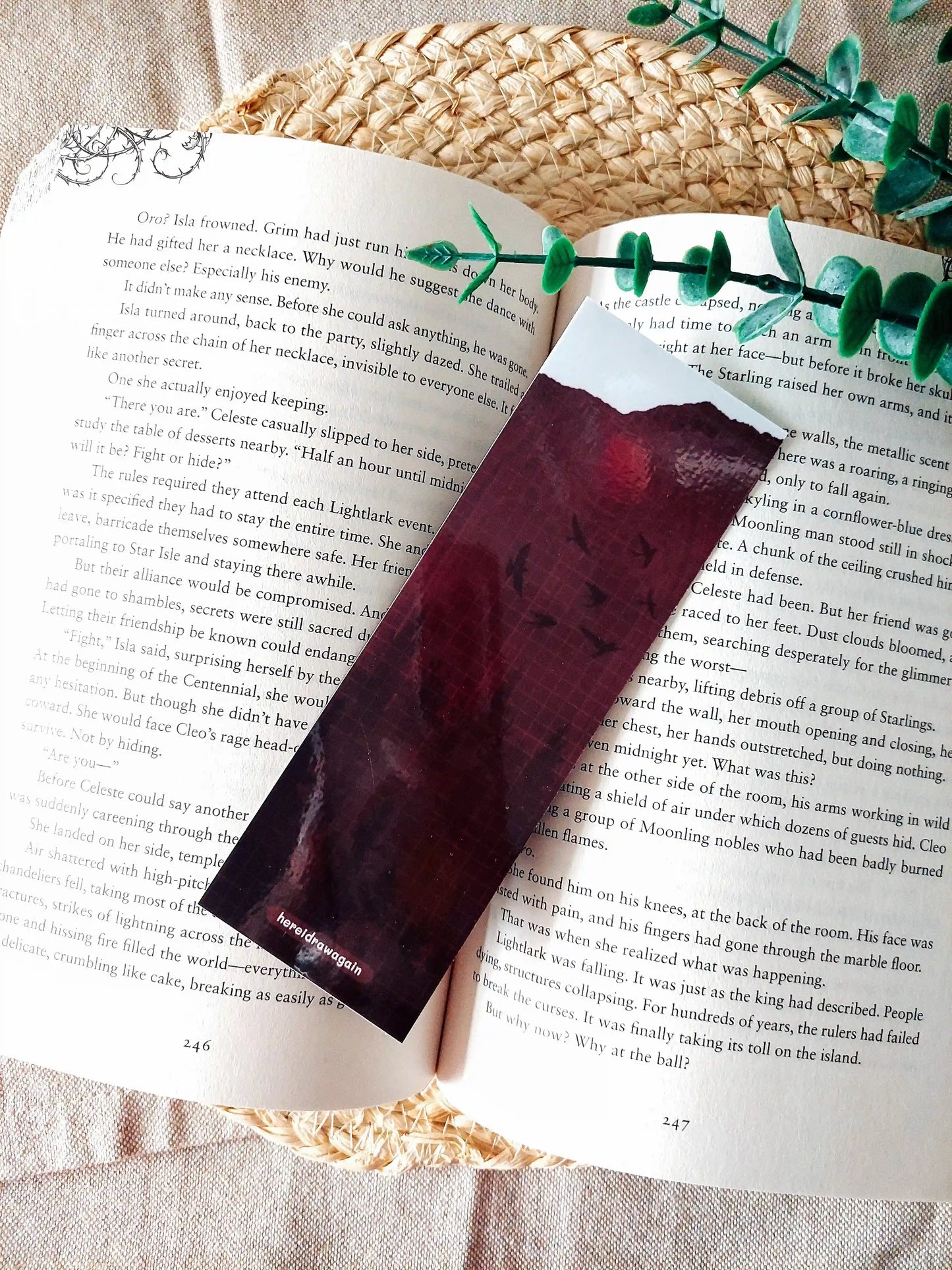 Back of the Nightshade bookmark placed on an open book, featuring a dark burgundy background with flying birds, a crossword pattern with book-related words. 