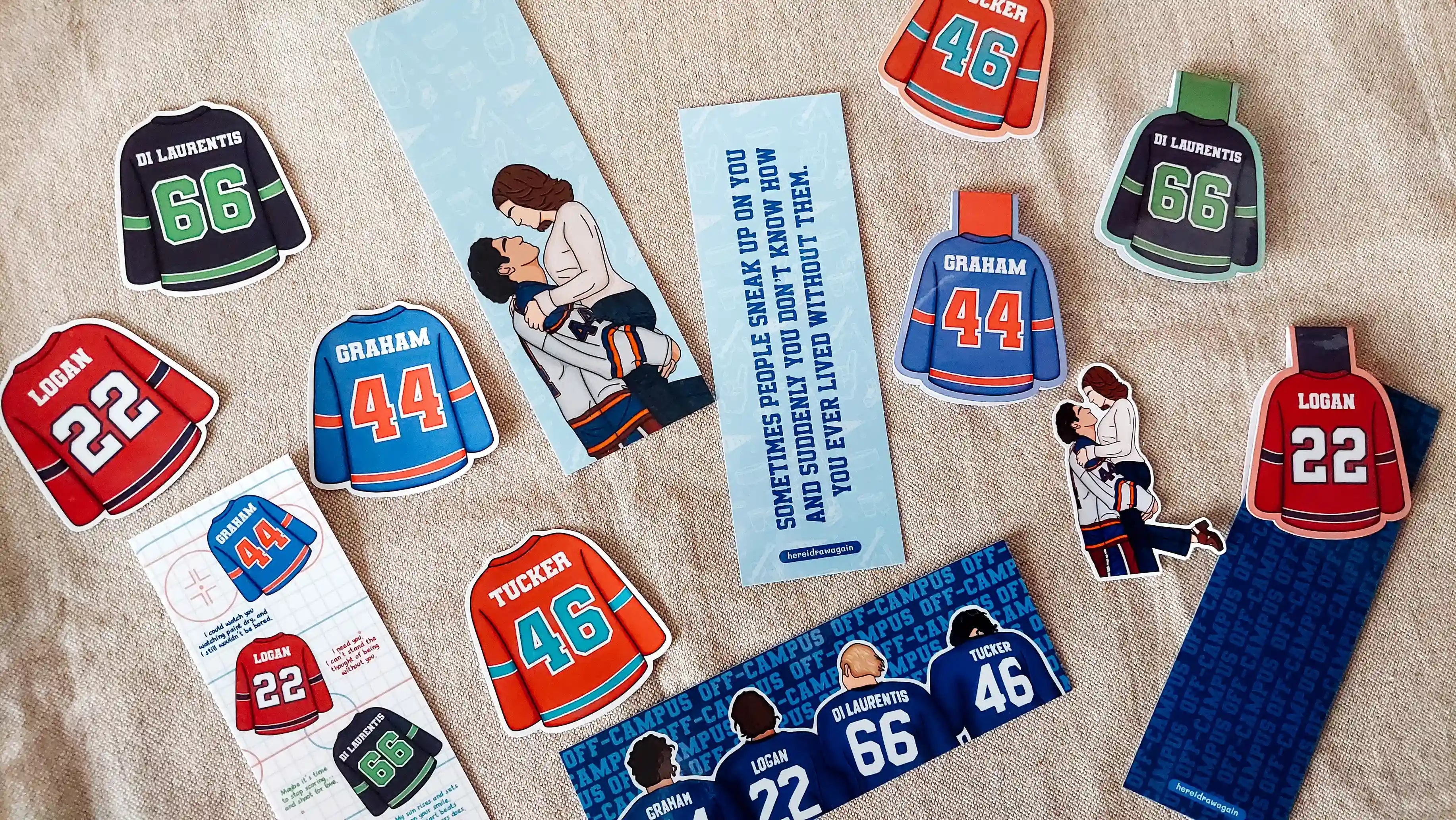 A flat-lay arrangement of Off Campus themed bookmarks and stickers featuring charcter jerseys and illustrations, displayed on a textured beige fabric background.