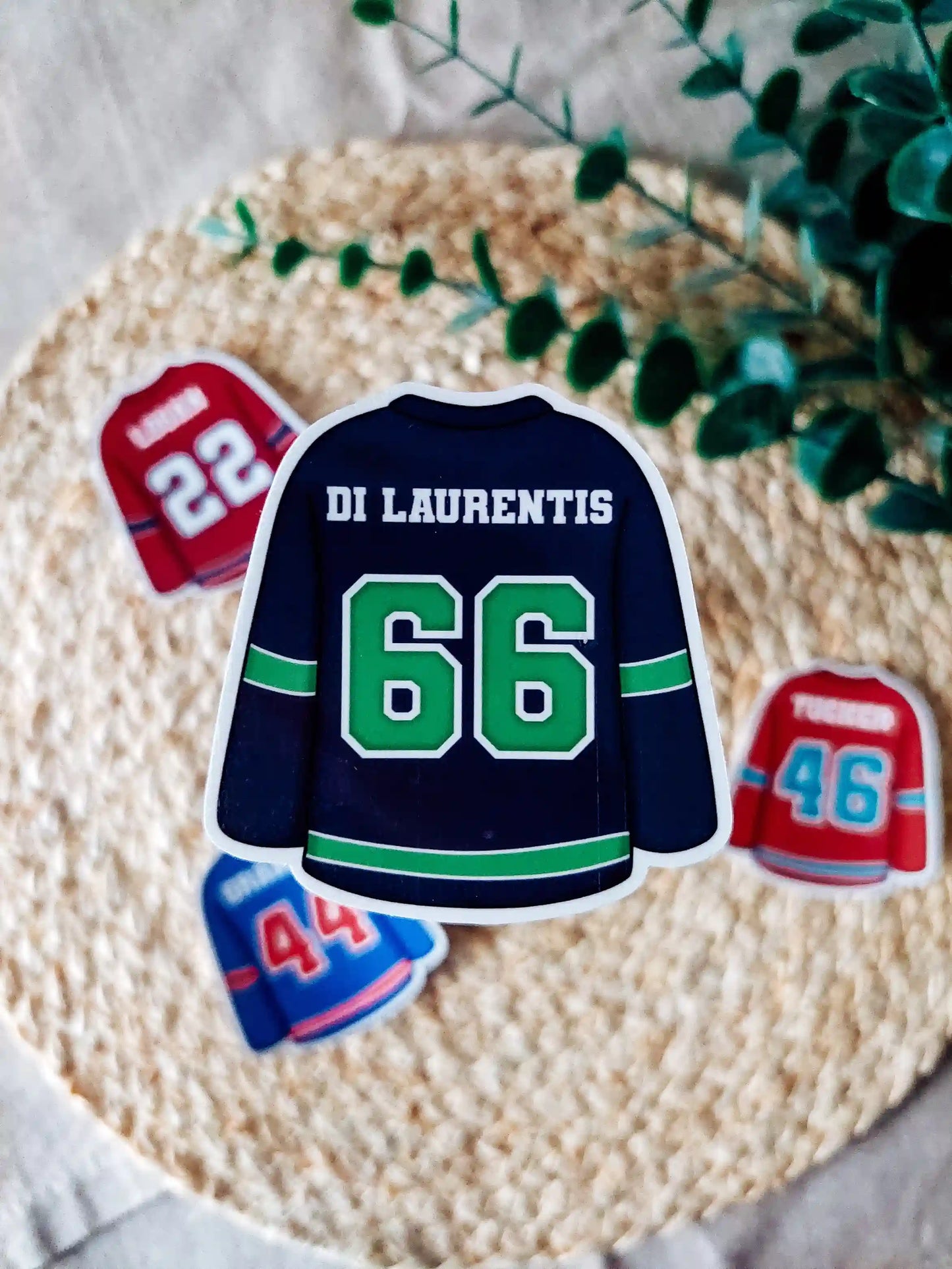 Off Campus inspired navy hockey jersey with "Di Laurentis 66" on it, placed on a textured surface with greenery.