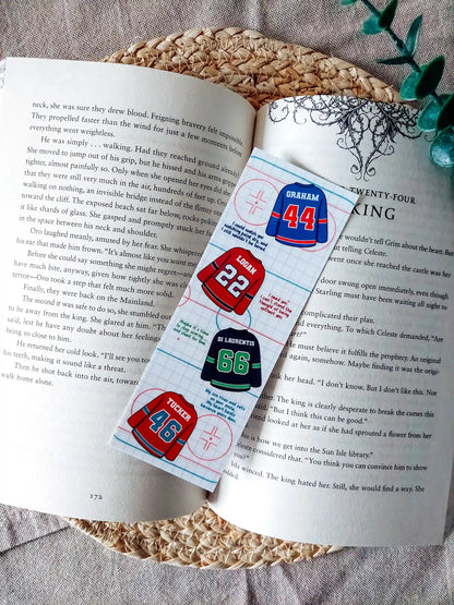 Off Campus inspired bookmark displayed on an open book, featuring "Graham 44", "Logan 22", "Di Laurentis 66" and "Tucker 46" jerseys with their quotes on a hockey rink patterned background.