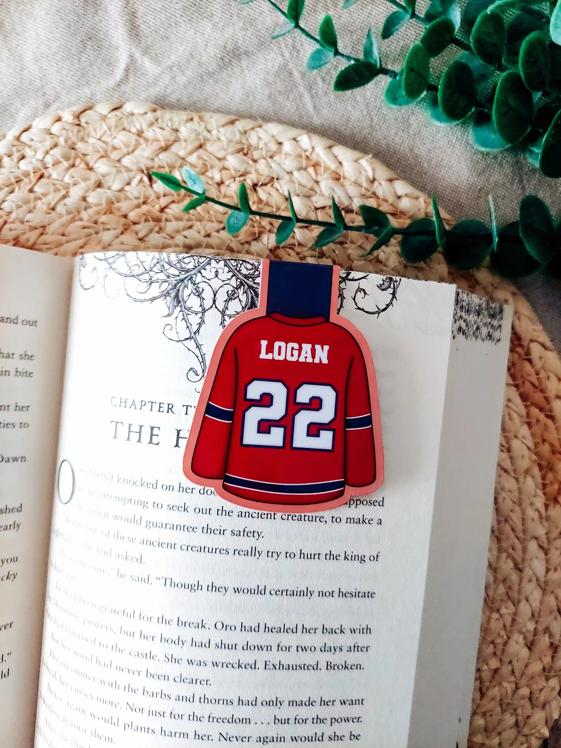 Off Campus inspired hockey jersey magnetic bookmark clipped onto an open book, showing the red and navy jersey design with "Logan 22" on the back.
