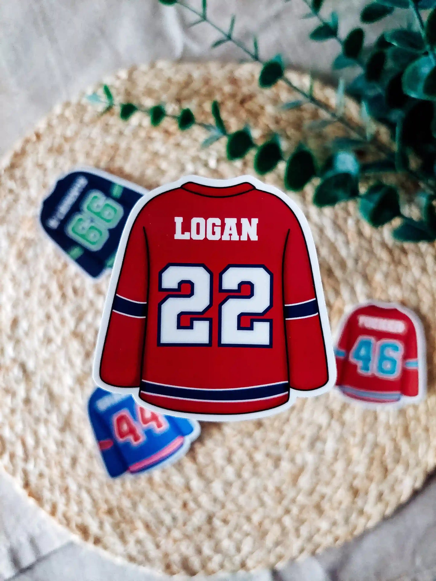 Off Campus inspired red hockey jersey with "Logan 22" on it, placed on a textured surface with greenery.