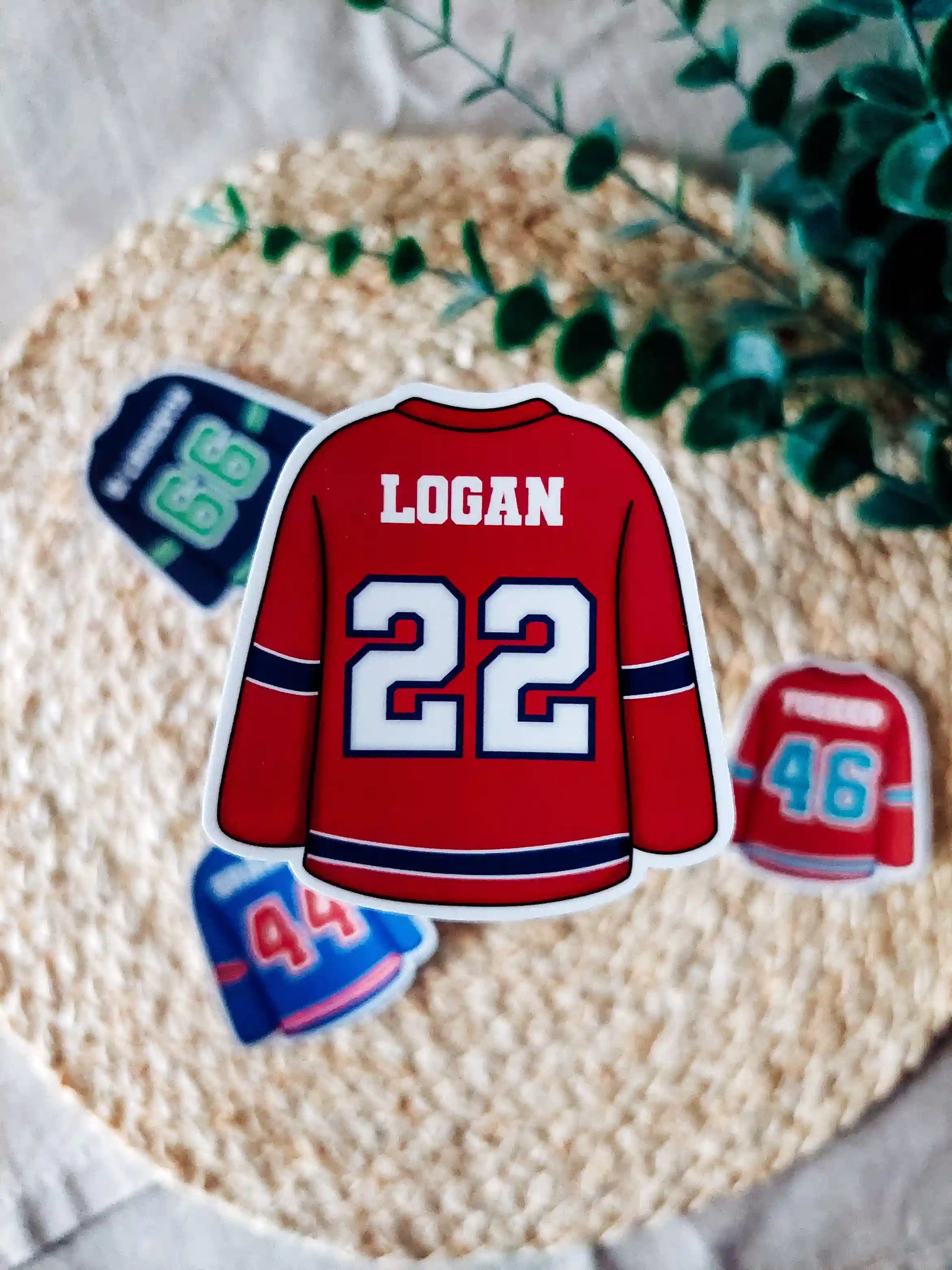Off Campus inspired red hockey jersey with "Logan 22" on it, placed on a textured surface with greenery.