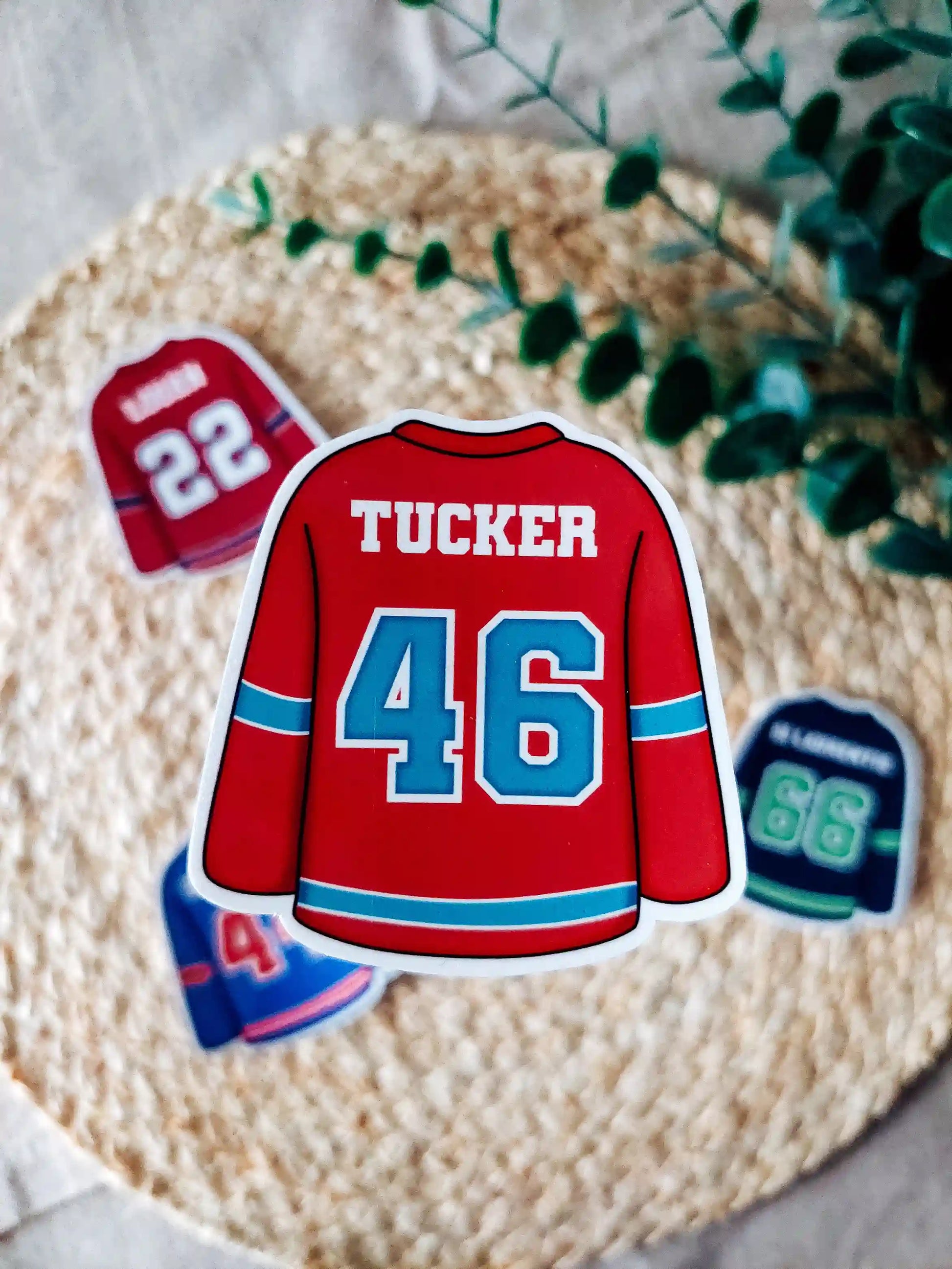 Off Campus inspired red hockey jersey with "Tucker 46" on it, placed on a textured surface with greenery.