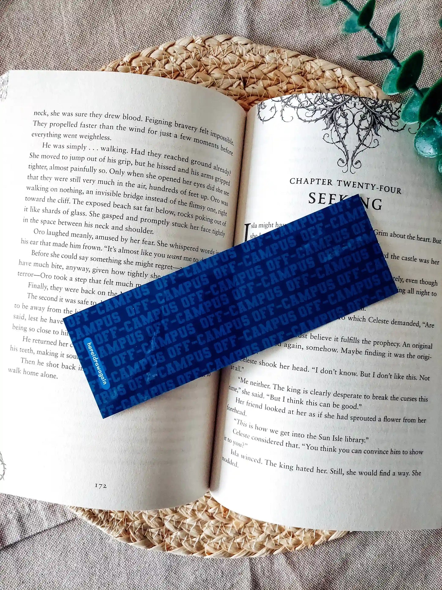 Off Campus inspired bookmark displayed on an open book, featuring a blue Off Campus text pattern on the back.