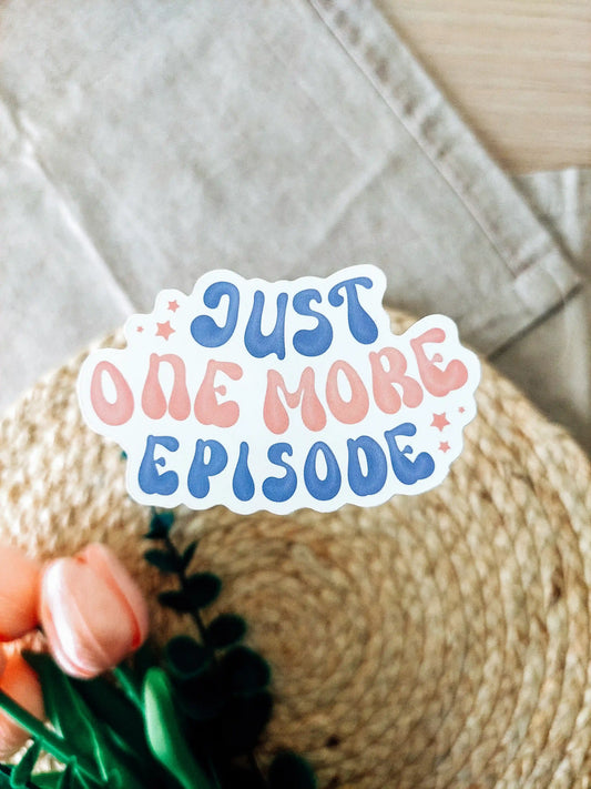 Vinyl sticker of the phrase "Just one more episode" in blue and pink lettering, photographed on a woven neutral background with pink tulips.