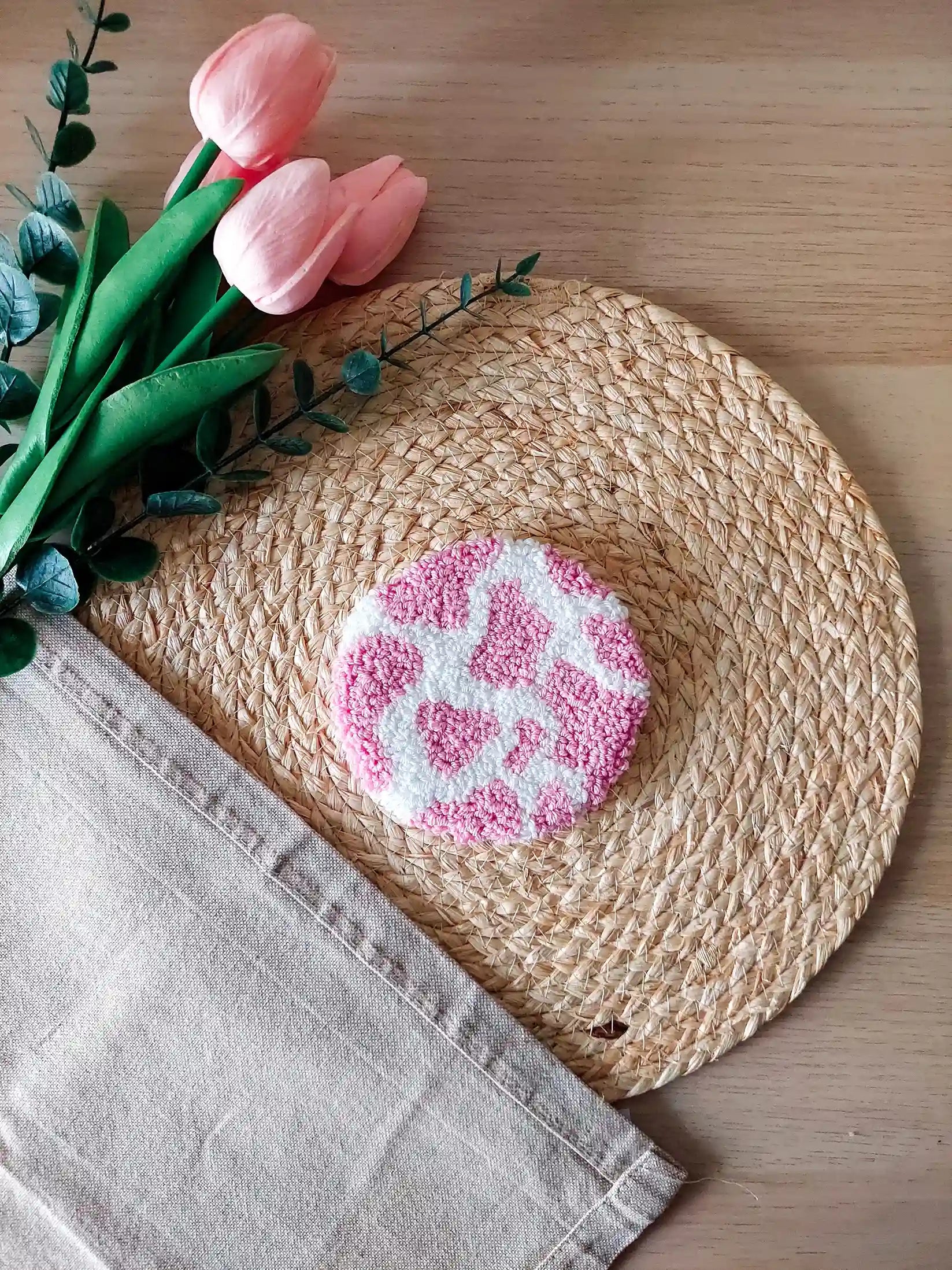 Handmade round punch needle coaster with a pink and white cow print. 