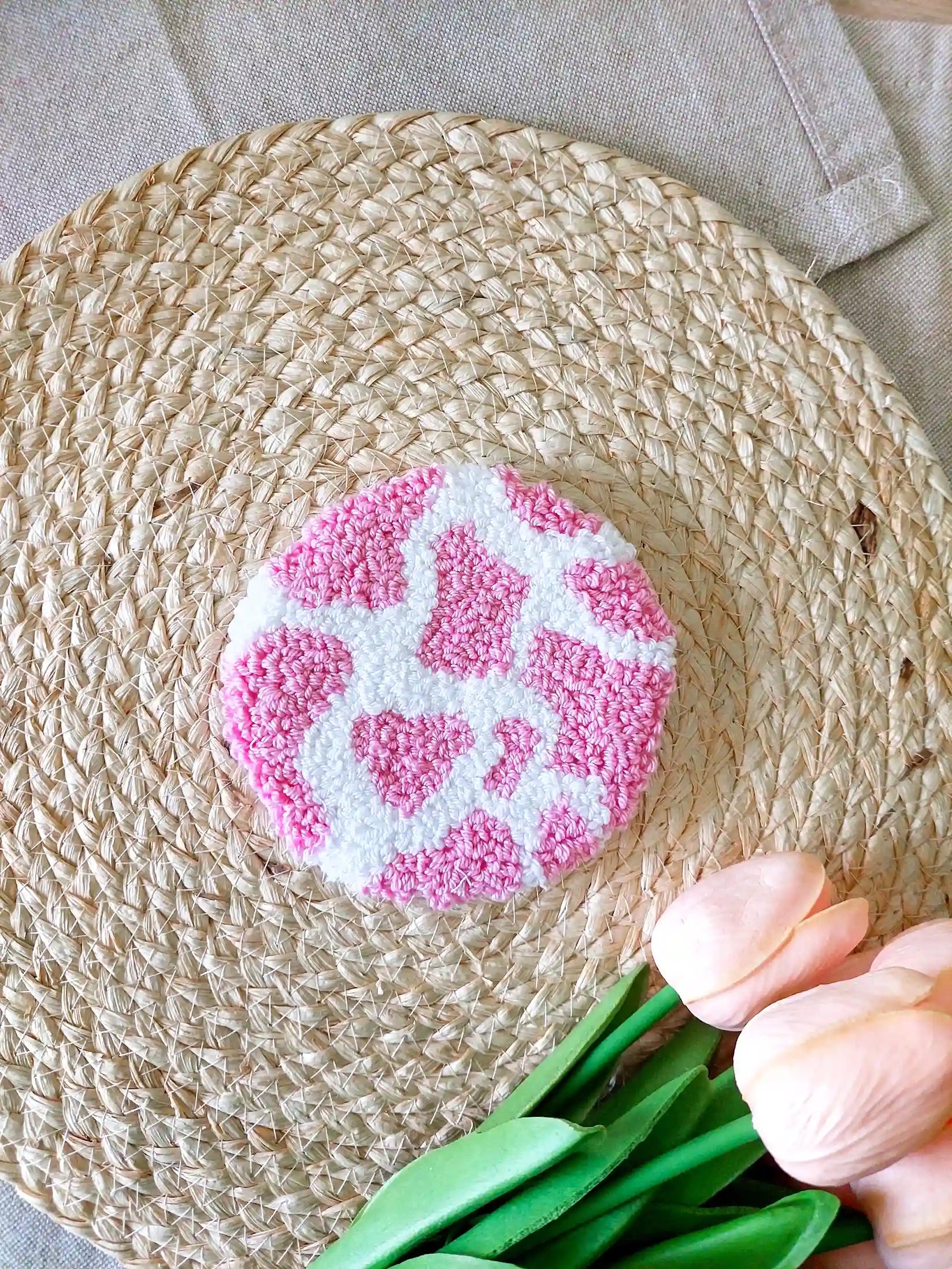 Handmade round punch needle coaster with a pink and white cow print. 