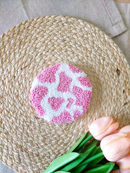 Handmade round punch needle coaster with a pink and white cow print. 
