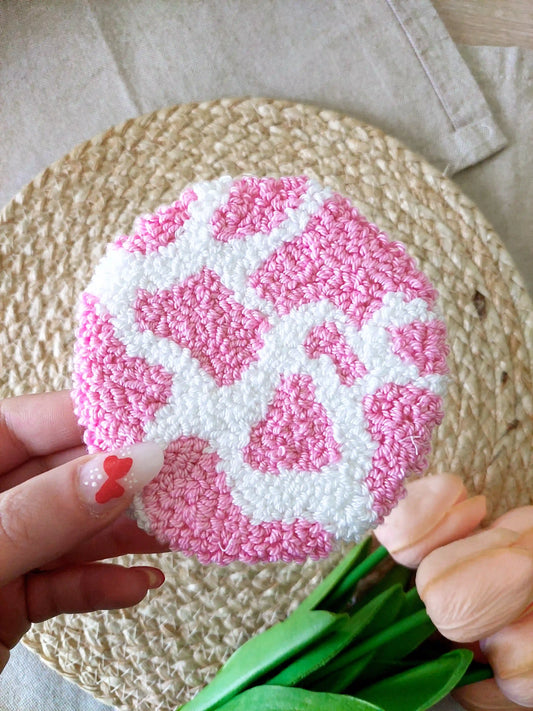 Handmade round punch needle coaster with a pink and white cow print. 