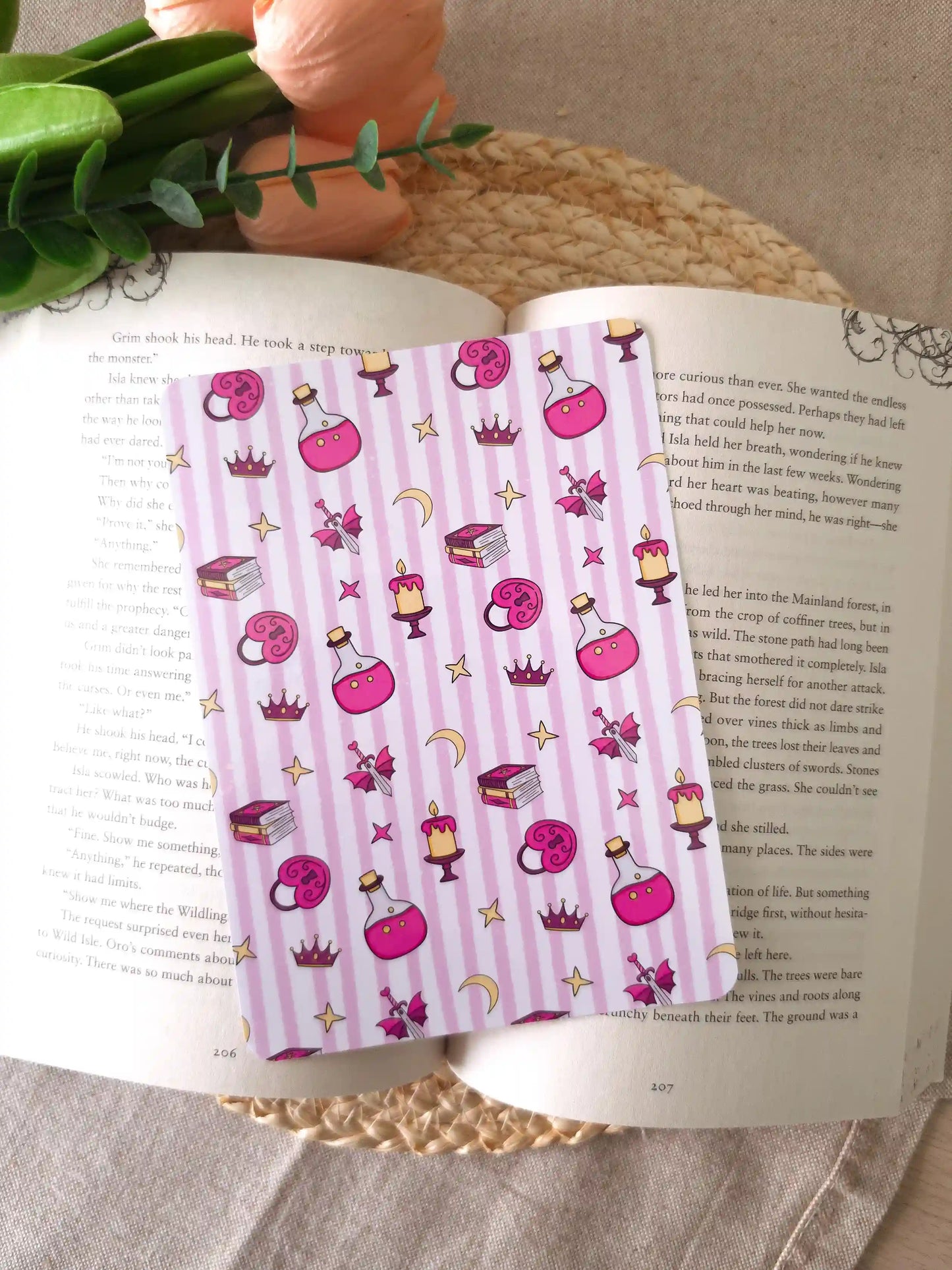 A pink and white striped ebook reader insert with a whimsical pattern of pink books, potion bottles, candles, stars, and crowns, shown resting on an open book.
