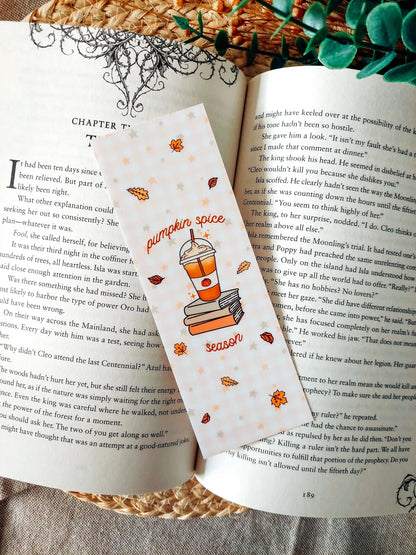Illustrated bookmark with the text "Pumpkin Spice Season", featuring an autumn-themed illustration of a pumpkin spice drink on stacked books, placed on an open book with a decorative background.