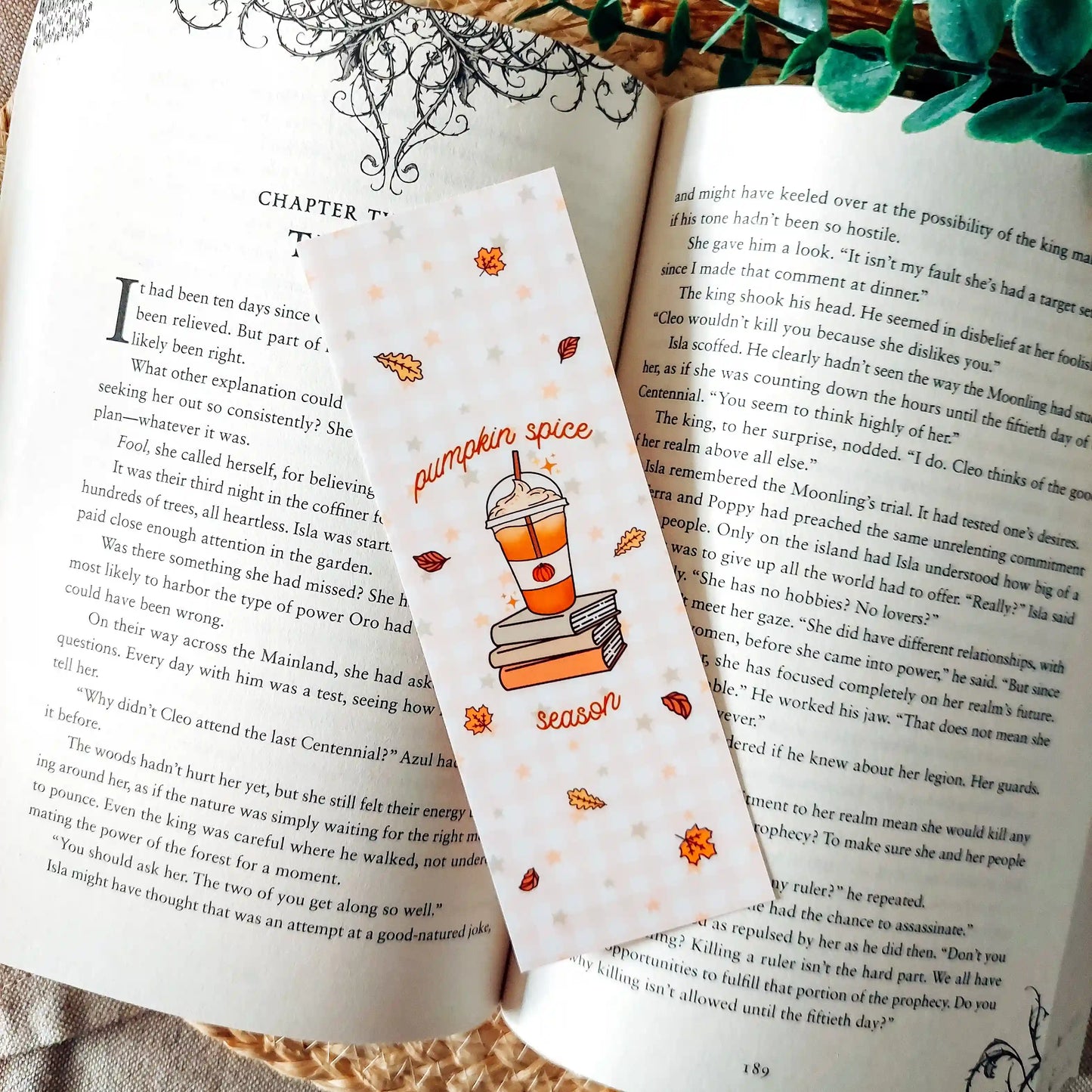 Illustrated bookmark with the text "Pumpkin Spice Season", featuring an autumn-themed illustration of a pumpkin spice drink on stacked books, placed on an open book with a decorative background.