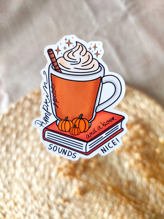 Vinyl sticker featuring an orange mug with whipped cream on top of a red book with small pumpkins and the tex "Pumpkin spice and a book sounds nice", photographed on neutral fabric background with woven mat.
