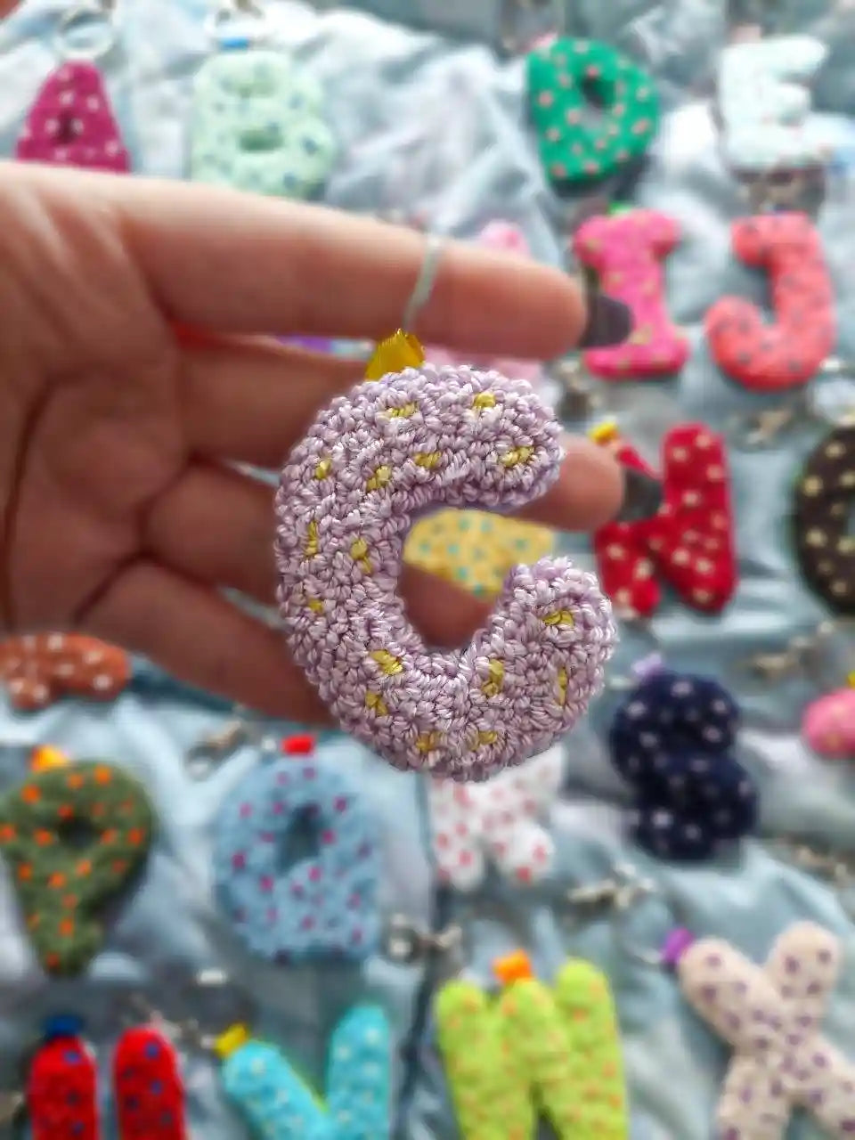 Hand holding a lilac and yellow letter "C" keychain.