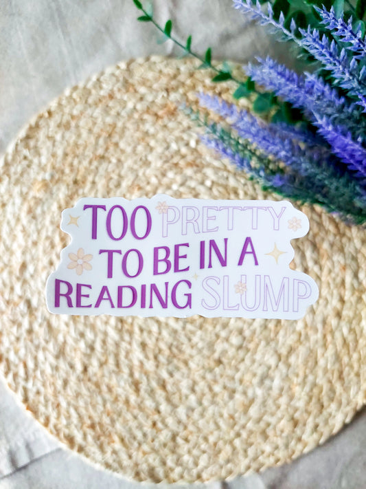 "Too Pretty To Be In A Reading Slump" sticker featuring purple and lilac text with small flowers and stars details on a woven background.