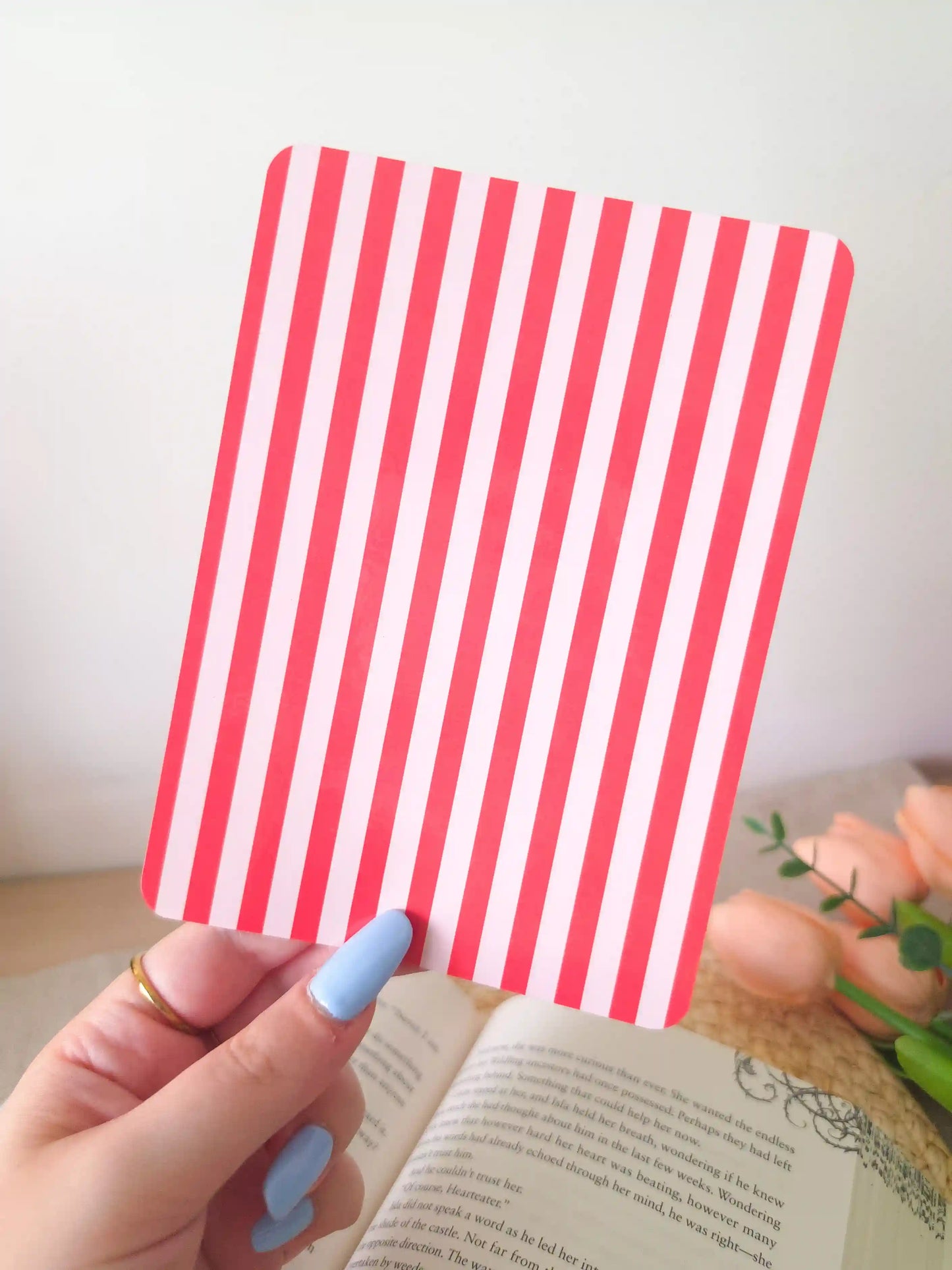 A hand holding an e-reader insert with bold red and light pink vertical stripes.