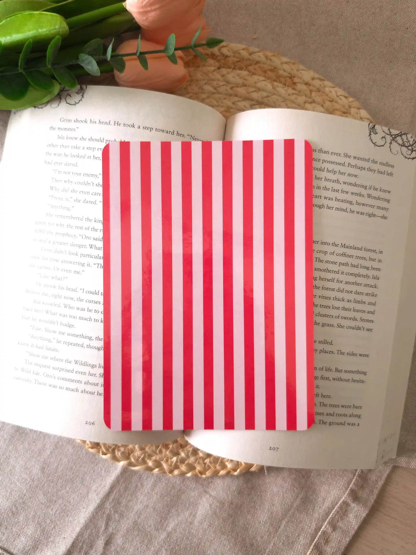 An e-reader insert with bold red and light pink vertical stripes, placed on an open book resting on a woven rattan mat.