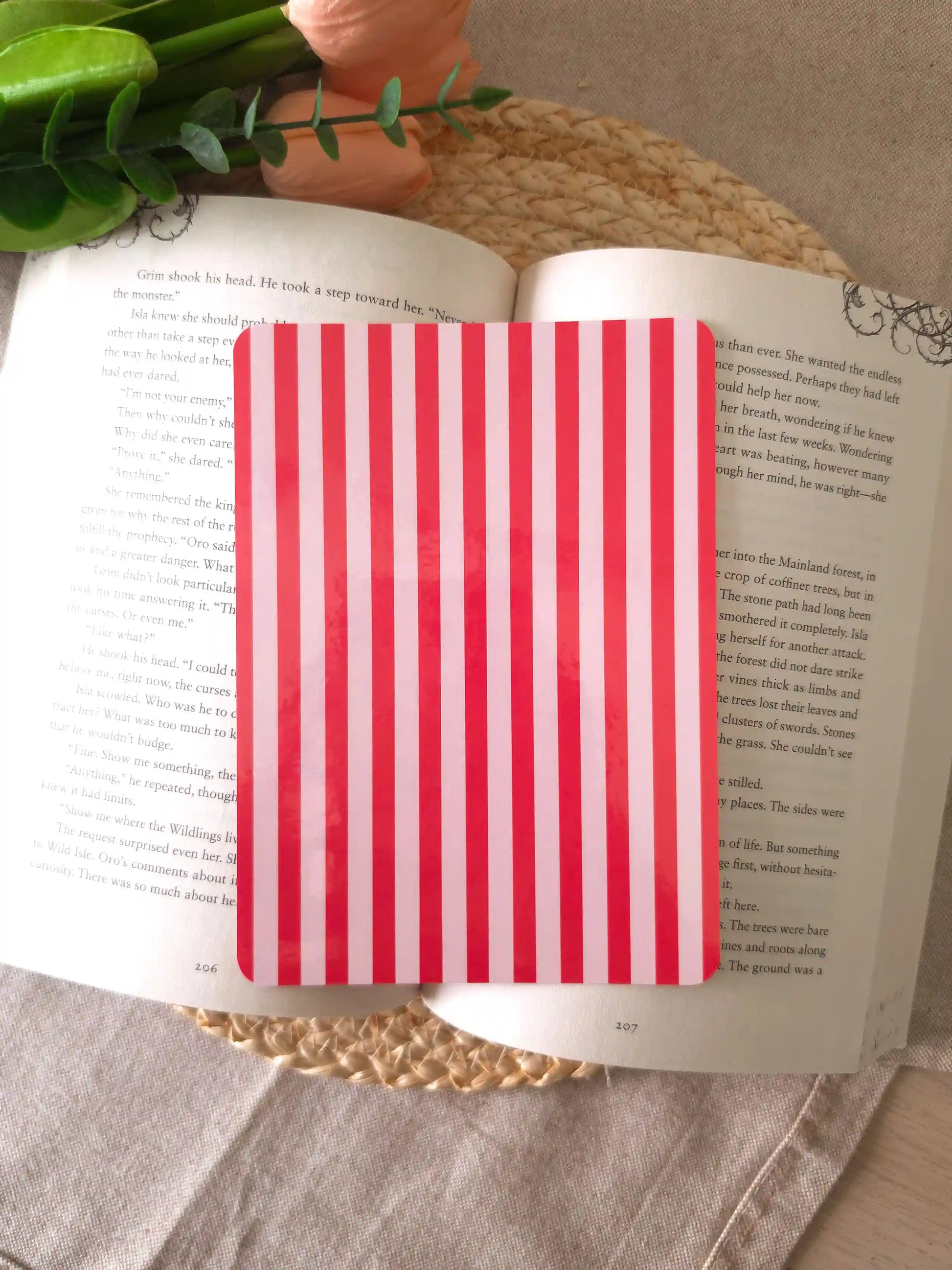 An e-reader insert with bold red and light pink vertical stripes, placed on an open book resting on a woven rattan mat.