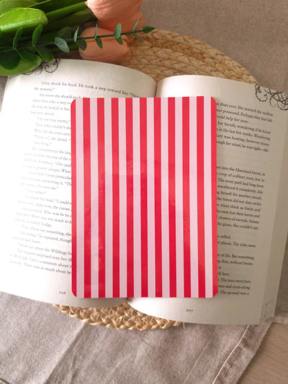 An e-reader insert with bold red and light pink vertical stripes, placed on an open book resting on a woven rattan mat.