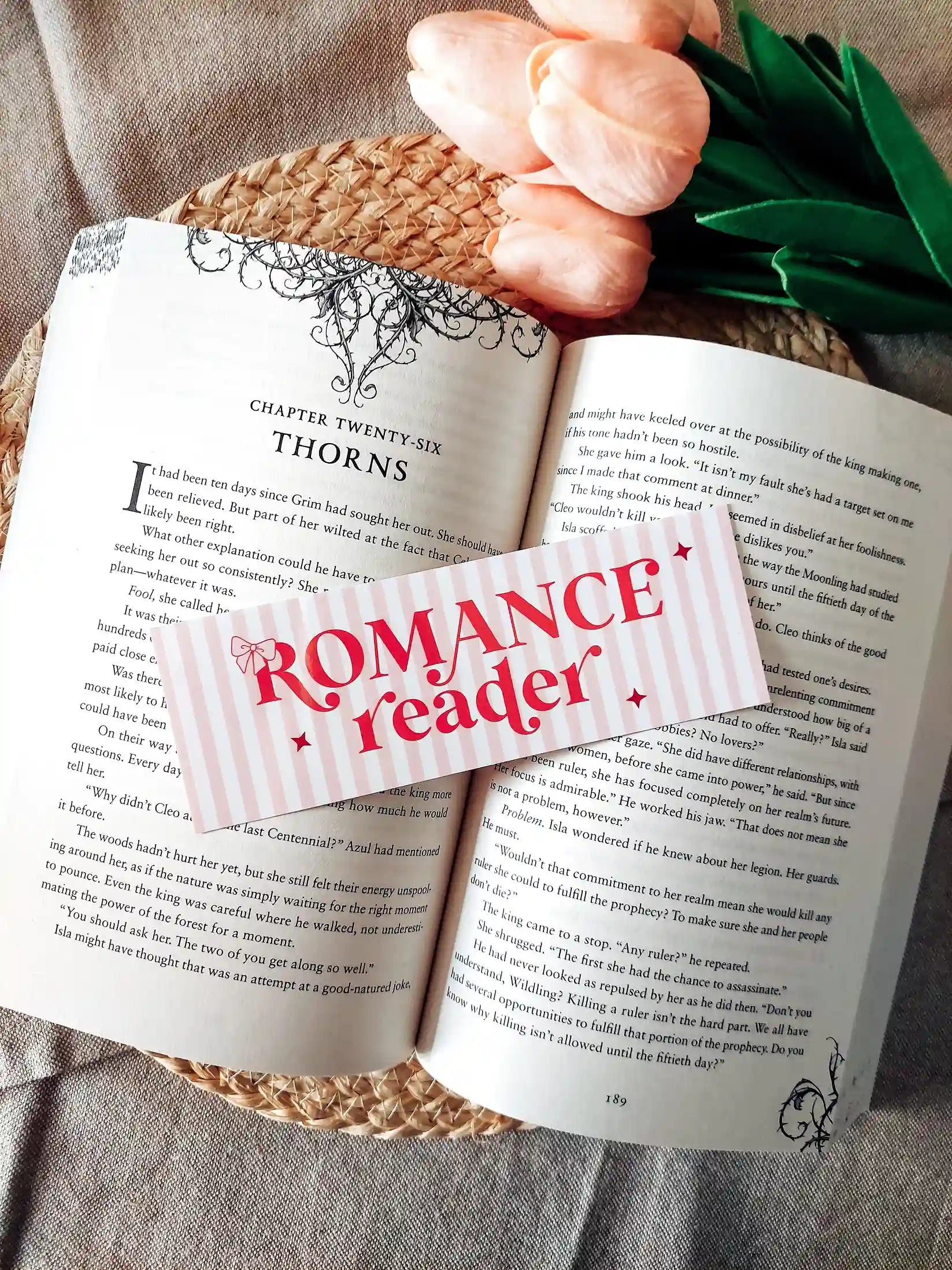 Illustrated bookmark with the text "Romance reader", featuring pink stripes and decorative stars, resting on an open book.