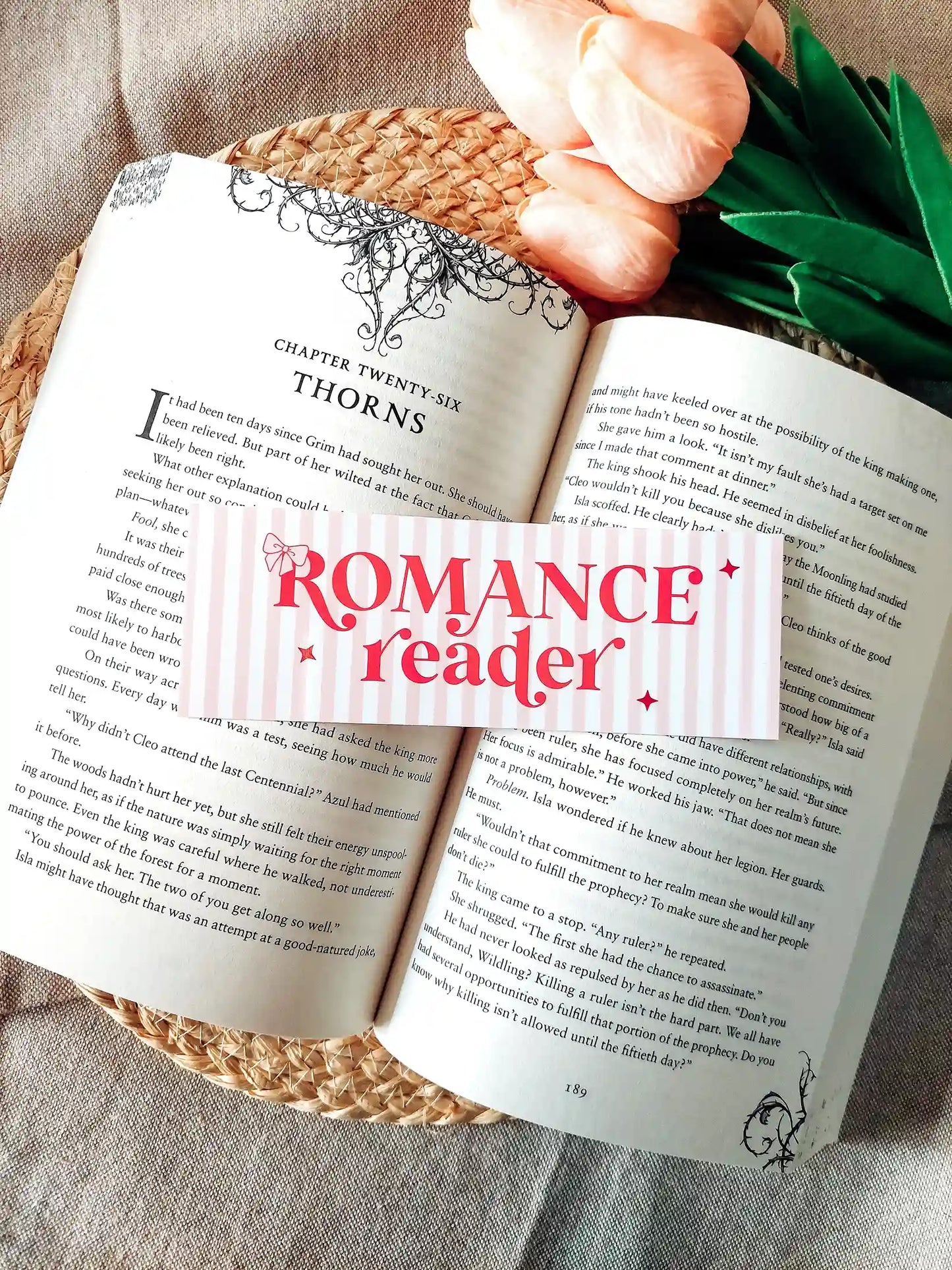 Illustrated bookmark with the text "Romance reader", featuring pink stripes and decorative stars, resting on an open book.
