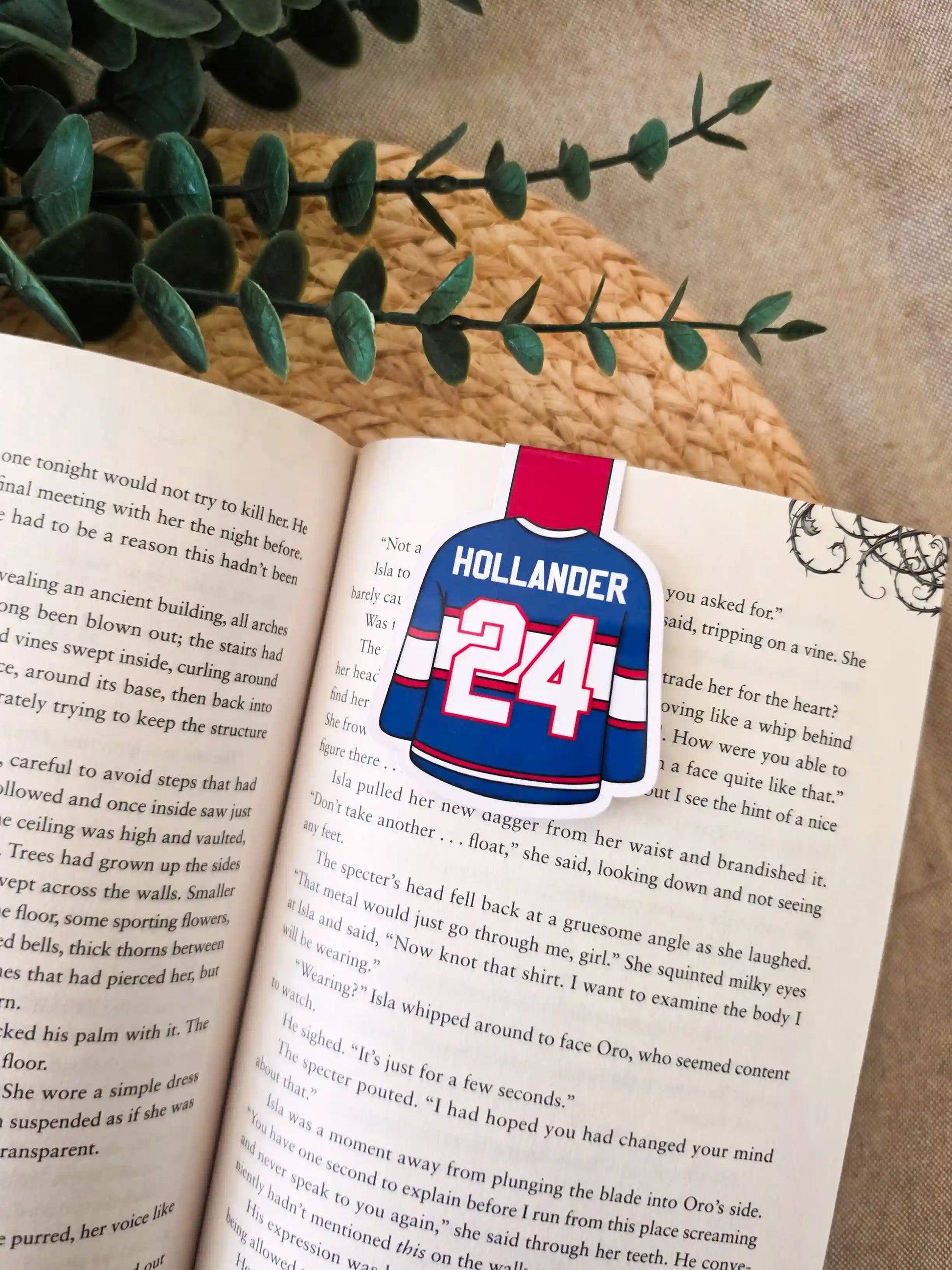 Heated Rivalry inspired hockey jersey magnetic bookmark clipped onto an open book, showing the blue and red jersey design with "Holllander 24" on the back.