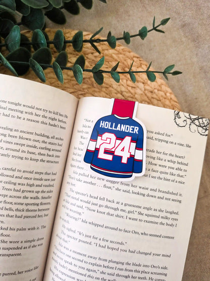 Heated Rivalry inspired hockey jersey magnetic bookmark clipped onto an open book, showing the blue and red jersey design with "Holllander 24" on the back.
