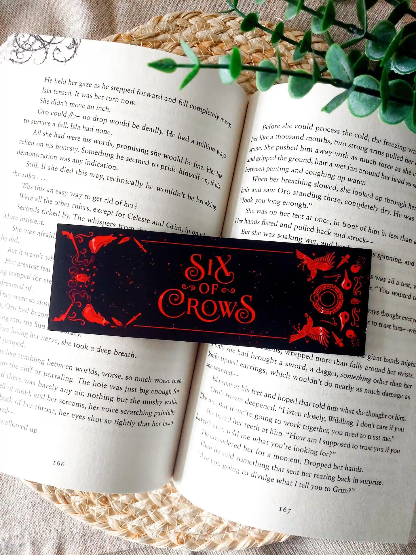 Bookmark inspired by the Six of Crows collector edition, featuring the quote "The heart is an arrow. It demands aim to land true." in red on a black background, resting on an open book.