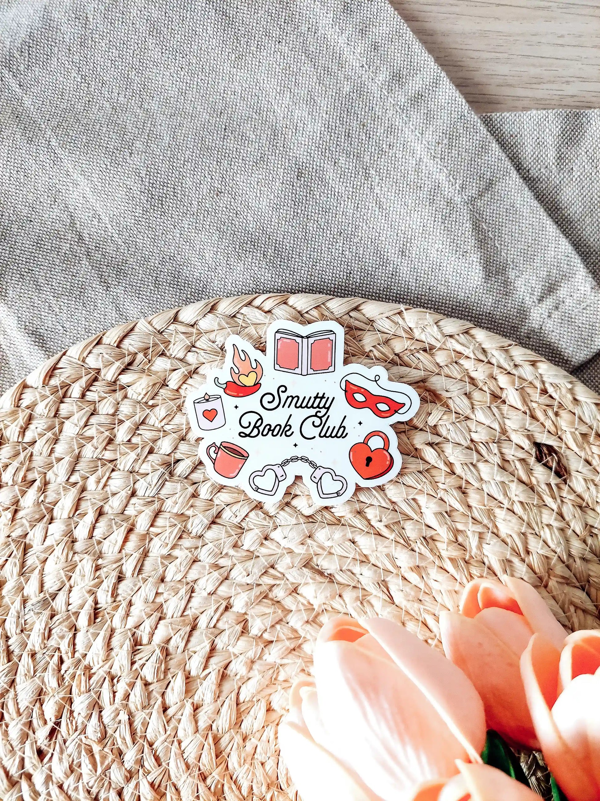 Vinyl sticker with the text "Smutty Book Club" surrounded by romance-themed illustrations including handcuffs, mask, heart lock.