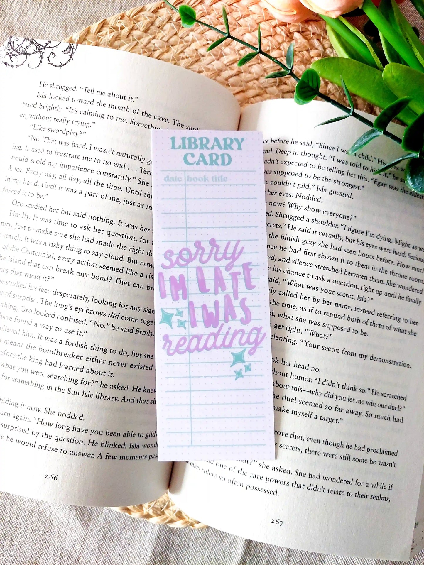 Bookmark designed like a library card with pastel colors and the text "Sorry I'm late, I was reading", placed on an open book.