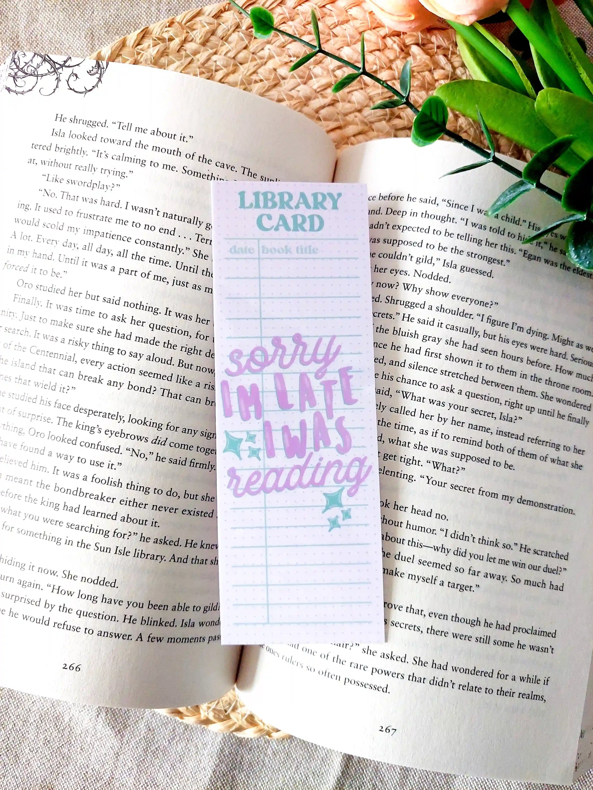 Bookmark designed like a library card with pastel colors and the text "Sorry I'm late, I was reading", placed on an open book.