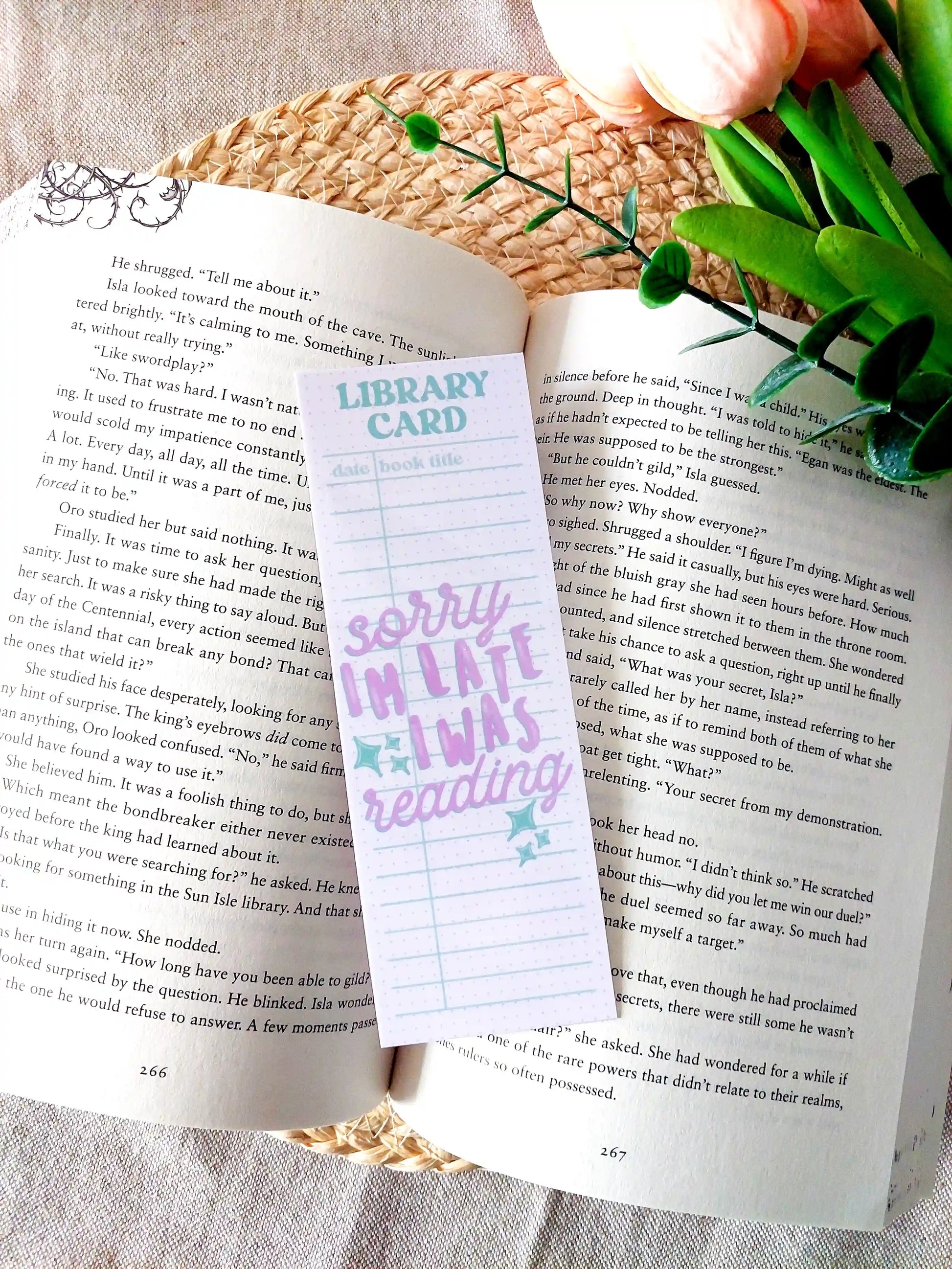 Bookmark designed like a library card with pastel colors and the text "Sorry I'm late, I was reading", placed on an open book.