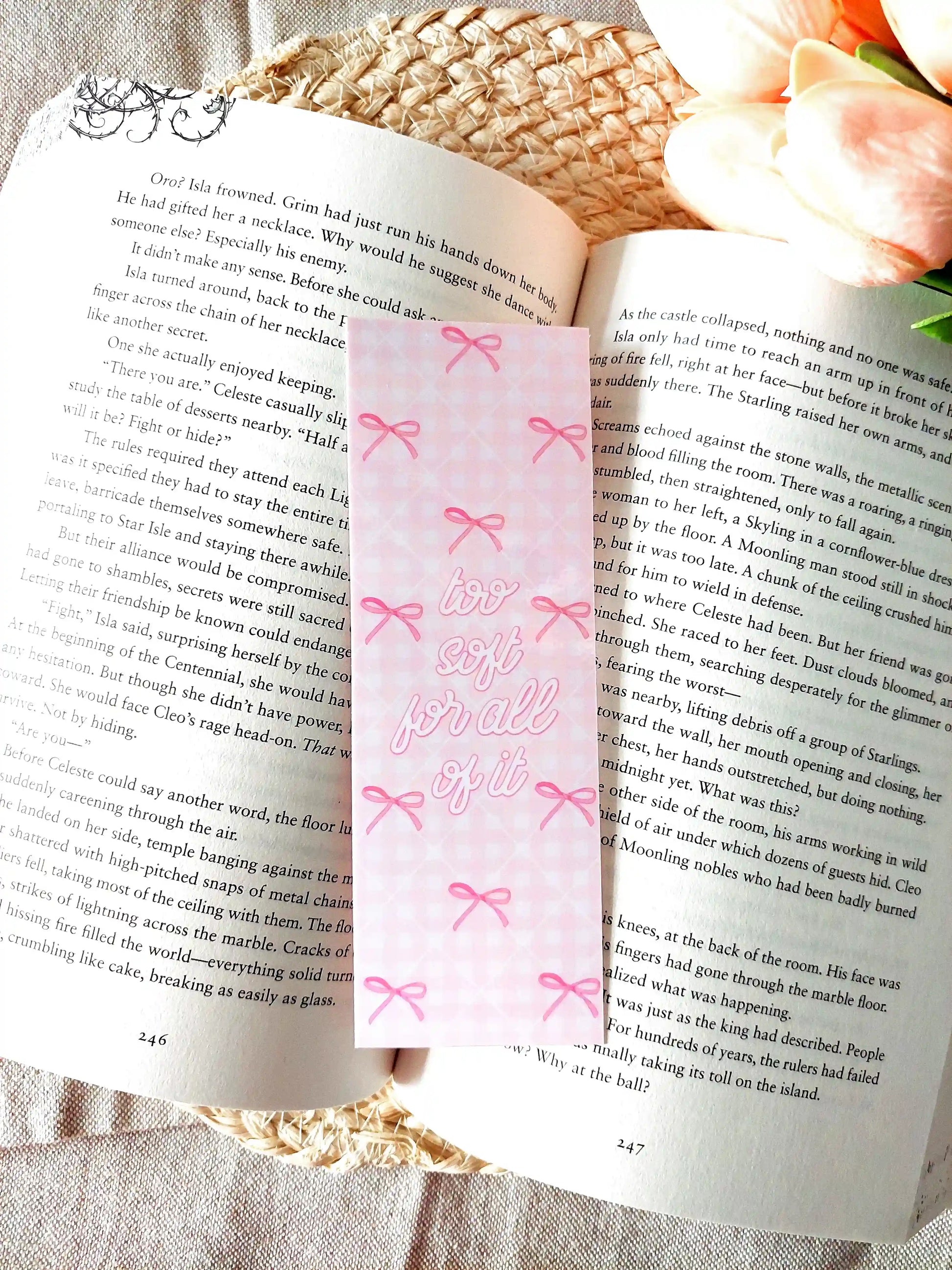 "Too Soft For All Of It" bookmark placed on an open book, featuring a pink floral pattern with bows and pink script text.