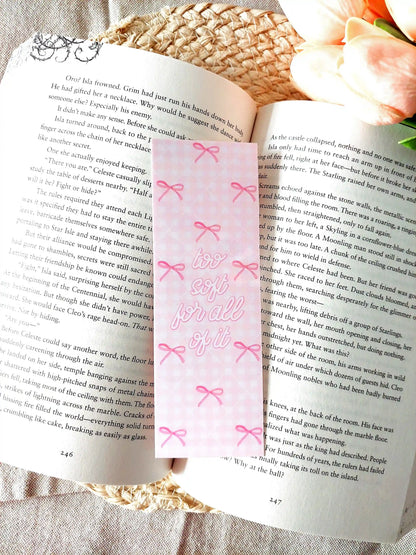 "Too Soft For All Of It" bookmark placed on an open book, featuring a pink floral pattern with bows and pink script text.