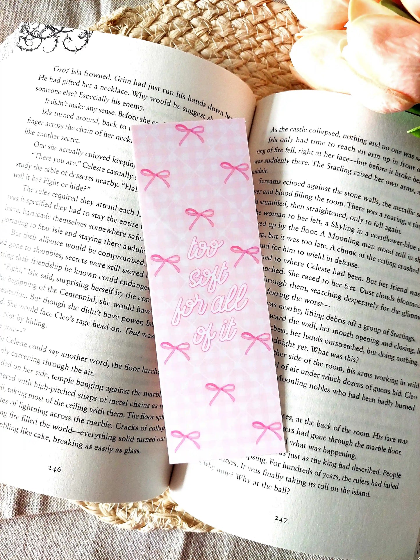 "Too Soft For All Of It" bookmark placed on an open book, featuring a pink floral pattern with bows and pink script text.