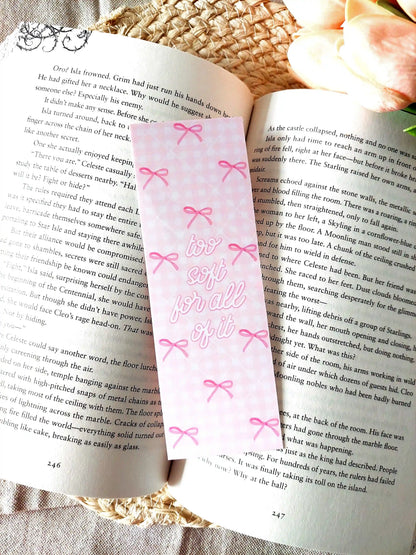 "Too Soft For All Of It" bookmark placed on an open book, featuring a pink floral pattern with bows and pink script text.
