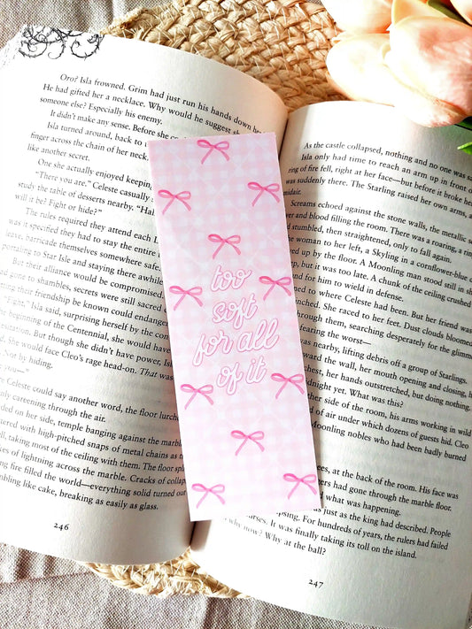 "Too Soft For All Of It" bookmark placed on an open book, featuring a pink floral pattern with bows and pink script text.