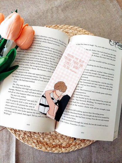 Bookmark inspired by The Summer I Turned Pretty, featuring Belly and Jeremiah with the quote "You’re my best friend. There are times I want to be more." on a pink gingham background, resting on an open book.