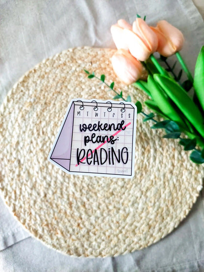 "Weekend Plans Reading" sticker on a rattan placemat, designed as a weekly calendar with black text and a line across it.