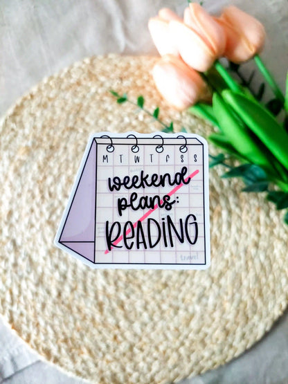 "Weekend Plans Reading" sticker on a rattan placemat, designed as a weekly calendar with black text and a line across it.