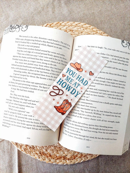 Bookmark with the text "You Had Me at Howdy", featuring a western-themed design with a cowboy hat, boots and rope on a soft gingham background, resting on an open book.