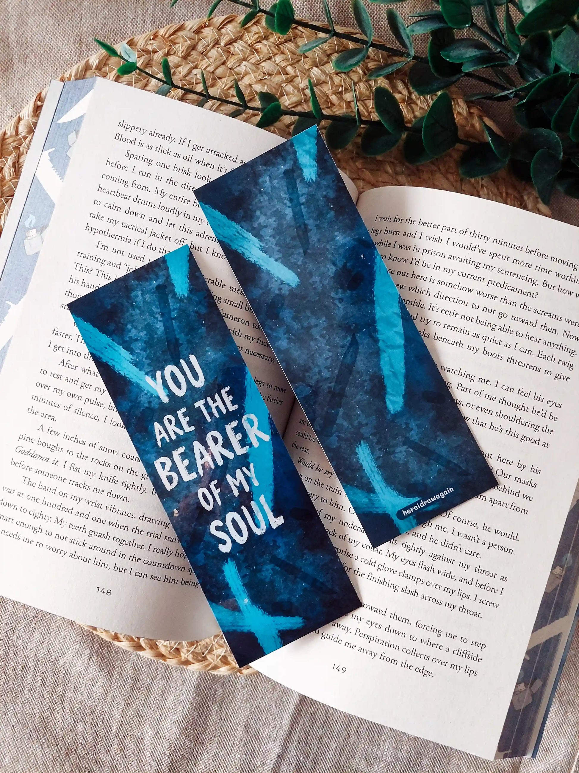 Your Knife, My Heart inspired bookmarks displayed on an open book, featuring a dark blue background with dagger illustrations and the quote "You are the bearer of my soul".